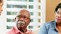 Healthcare provider speaking with an older adult patient and family caregiver at home, emphasizing communication in hospice care.