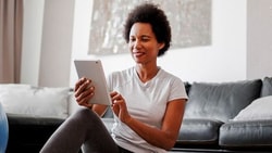 A person uses a tablet near a blue exercise ball in a living room.