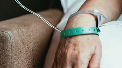 An arm with an IV line and medbridge wristbands on a bed.