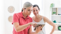 Two women indoors use a tablet, showing how hybrid care with medbridge supports patient interactions.