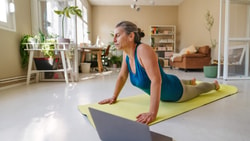 Older woman doing prone press-up exercise on a yoga mat while following a lumbar radiculopathy treatment program online.