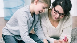 A woman and a boy make crafts with colorful paper and glue.