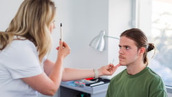 A healthcare worker uses a penlight for an eye exam on a seated person in a well-lit room.