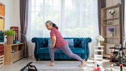 An older adult woman performs her prescribed exercises in her living room.