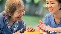 Occupational therapist supporting an older adult in a craft activity, demonstrating motor learning strategies after stroke.