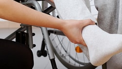 A Medbridge caregiver helps a wheelchair user by holding their leg in light gray sweatpants.