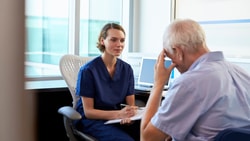 Clinician in scrubs listens attentively to older patient during evaluation, discussing symptoms of cognitive fatigue.
