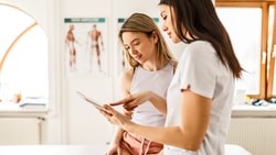 A healthcare provider shows a young woman information on a tablet in a medbridge exam room.