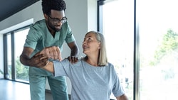 A physical therapist assisting a smiling older adult with arm exercises, demonstrating patient engagement best practices during rehabilitation for lateral elbow pain.