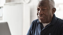 Older adult patient smiling while using a laptop for virtual care, representing digital tools that support patient engagement.