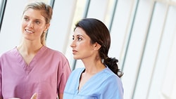 Three medbridge professionals in scrubs chat in a hallway with large windows.