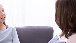 A girl with braces talks to a brown-haired woman in a bright room.