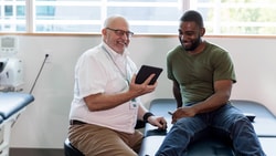 Doctor and patient smile at a tablet in a bright Medbridge exam room.
