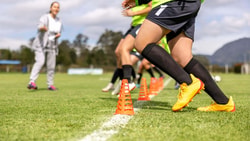 Soccer player executing cone drills on a field under coach supervision for sports injury prevention.