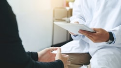 Clinician holds a tablet while consulting with a patient, capturing outcome data during an office visit
