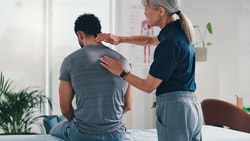 A woman examines a man’s back in a medical office, highlighting digital healthcare and medbridge.