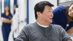 A smiling wheelchair user greets a healthcare worker in a busy medbridge hallway.