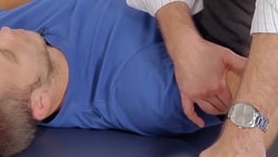 A person in a blue shirt receives shoulder therapy on a table.