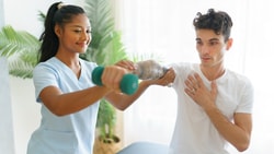Therapist guiding patient through shoulder rehab exercise for rotator cuff tendinopathy using a dumbbell.