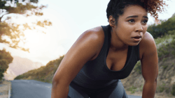 A jogger leans forward to catch her breath on a tree-lined rural road.