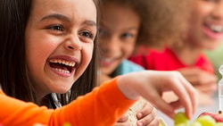 Children laughing together around a meal with water and carrots on the table.