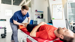 Clinician applying sports manual therapy with foam roller to athlete’s knee during rehab session.