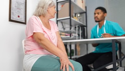 An older woman consults with a Medbridge professional in teal scrubs at a medical office.