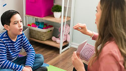 Speech-language pathologist works with a young boy on articulation during a stuttering therapy session.