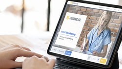 Laptop showing a healthcare-themed medbridge website with a doctor, beside a coffee cup and plant.