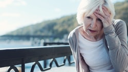 Person leaning on a railing outdoors, holding their head and appearing distressed.