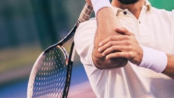Medbridge athlete in a white polo swings his racket on the tennis court.