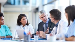 Medical professionals and a suited man discuss digital healthcare around a table in a bright office, referencing medbridge.