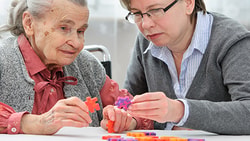 An elderly woman and a younger woman are assembling a colorful puzzle at a table.