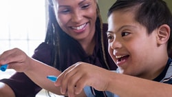 A woman and a child with Down syndrome smiling while crafting at a table.