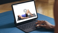 Person using a tablet to follow along with a home exercise program video on a yoga mat, illustrating HEP therapy.