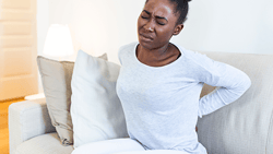A person on a couch holds their lower back in pain.