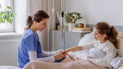 A home health nurse providing bedside care to a pediatric patient during an in-home visit.