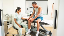 A healthcare professional uses medbridge software to examine a patient’s knee in a medical office.