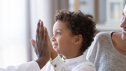 A child high-fives a Medbridge clinician with a smiling woman beside them.