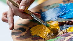 Hand blending yellow paint on a wooden palette with a paintbrush.