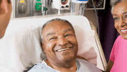 A Medbridge patient in bed smiles at a doctor and a woman.