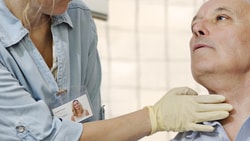 A healthcare professional in gloves examines an older man's neck in a clinic.