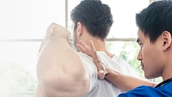 A healthcare professional assesses a patient's shoulder in a bright room.