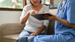 Home health nurse educates patient on using a JP drain color chart for post-surgical drainage monitoring.