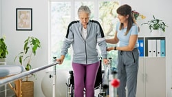 Therapist assisting a senior patient with gait training in parallel bars to address Unsteadiness on Feet (R26.81).