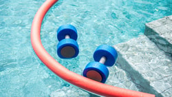 Aquatic therapy equipment in a pool, including foam dumbbells and a noodle, used to support pediatric exercise and conditioning.