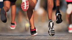 Group of runners' legs and sneakers moving on a paved road.
