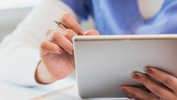 A Medbridge employee in a blue uniform uses a tablet with a stylus.