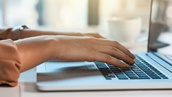 Typing on a laptop with a Medbridge coffee cup in the background.