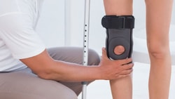 In a bright room, one person helps another with a knee brace as they stand with crutches, showcasing the medbridge product.